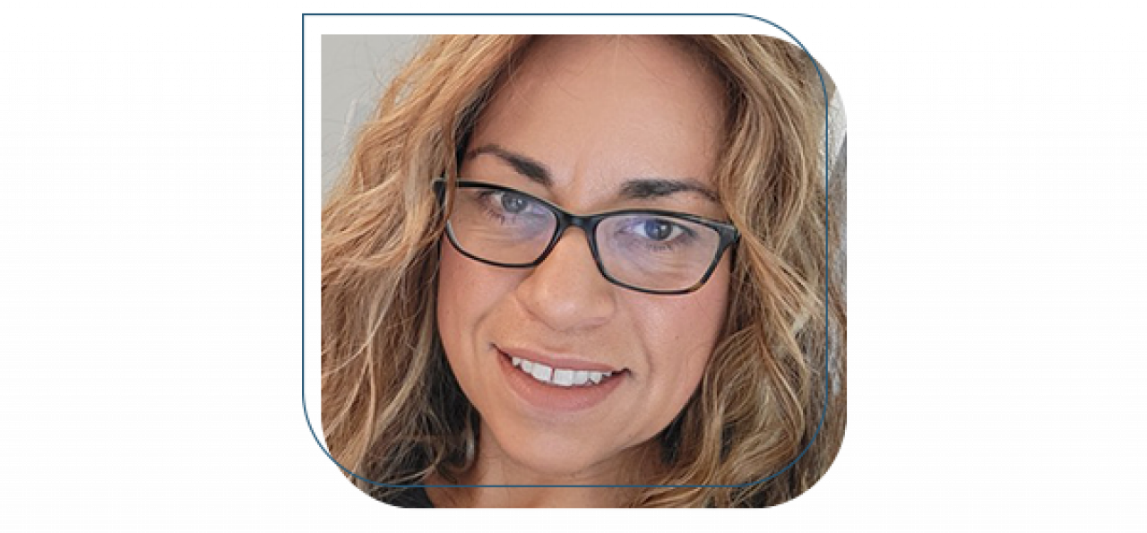 A woman wearing black-framed eyeglasses poses for a self photo. Her head and neck are visible, and she is smiling.