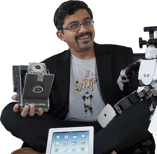 Faculty Shyam Sundar sits with an iPad, robot, and other technology
