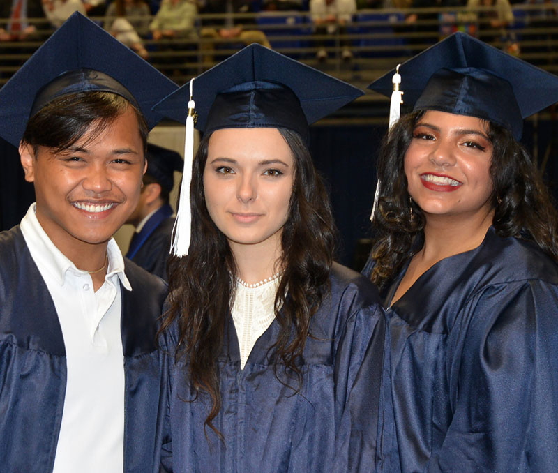 Two graduates in cap and gown smile for the camera.