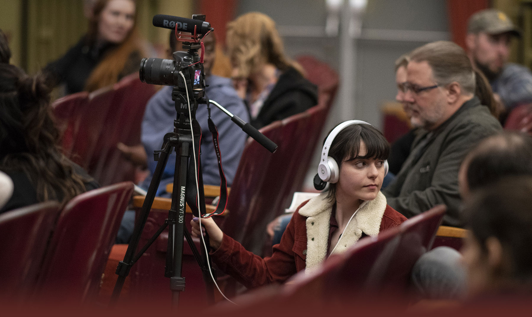 A student with headphones and a camera prepares to film a lecture.