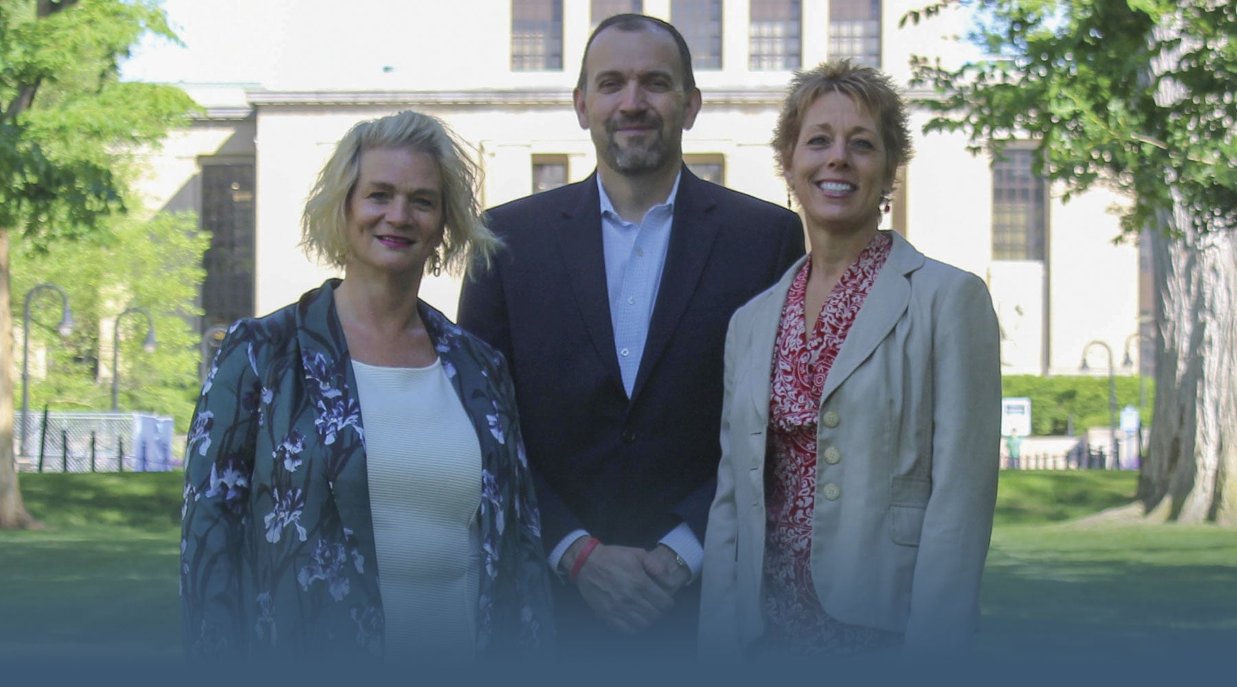 The Office of Internships and Career Services staff Stephanie Girouard, Assistant Dean Bob Martin, and Julie Miller pose on a sunny day in front of Pattee Library