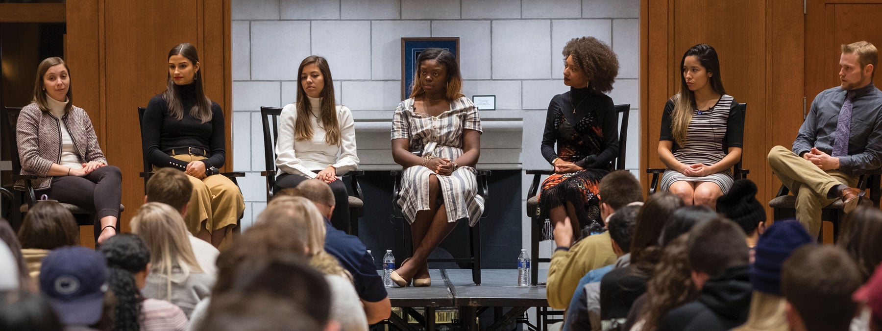 A panel of seven students sits in front of a crowd discussing career advice