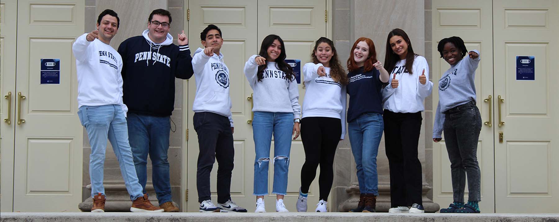 A student with a camera, shoulder-length curly brown hair, glasses and a Penn State sweatshirt, poses with her arms
outstretched to mimic the sculpture of five children playing on the lawn of the old president's house that is now part of the Hintz Family Alumni Center.