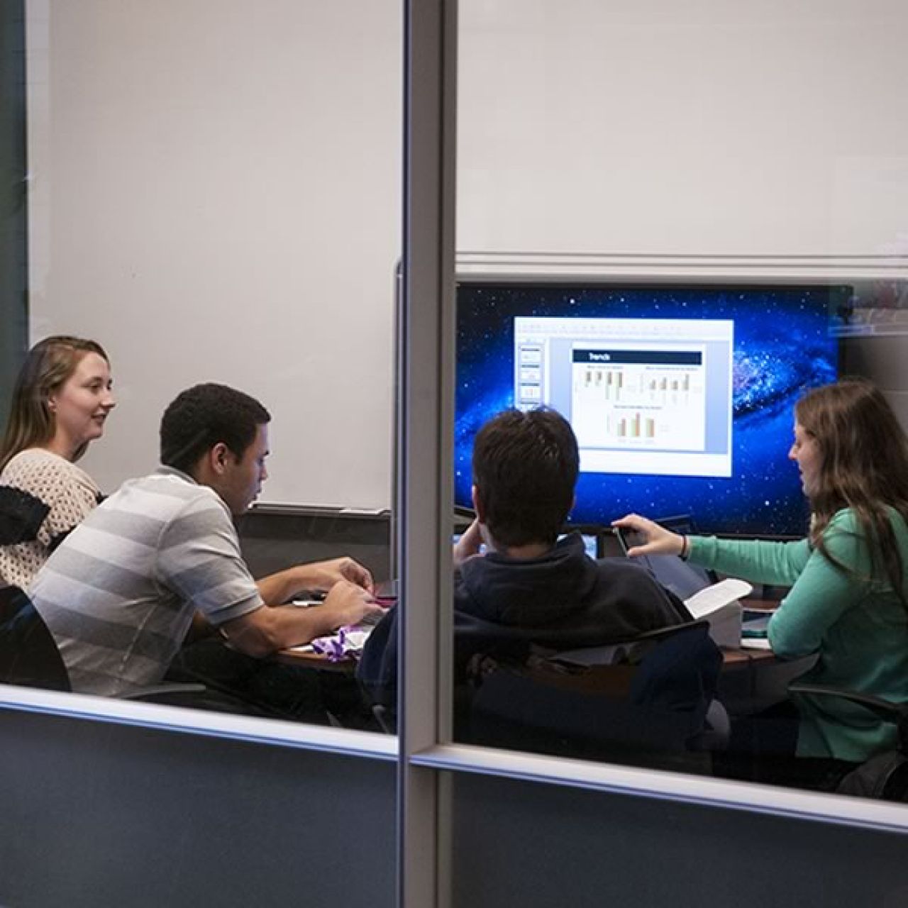 A group of four students sitting in front of a large monitor working on a group project