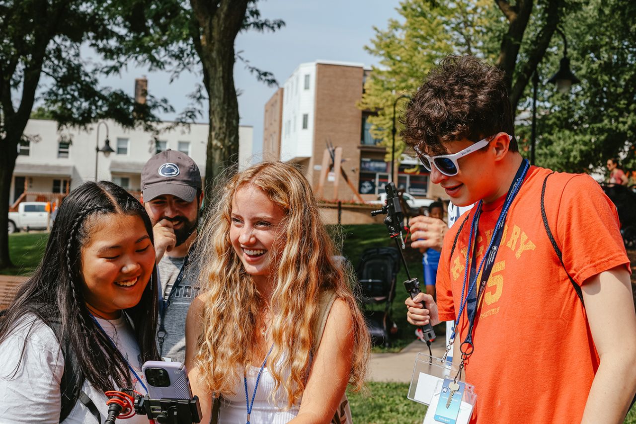 Three students walk while holding smartphones and camera holders.