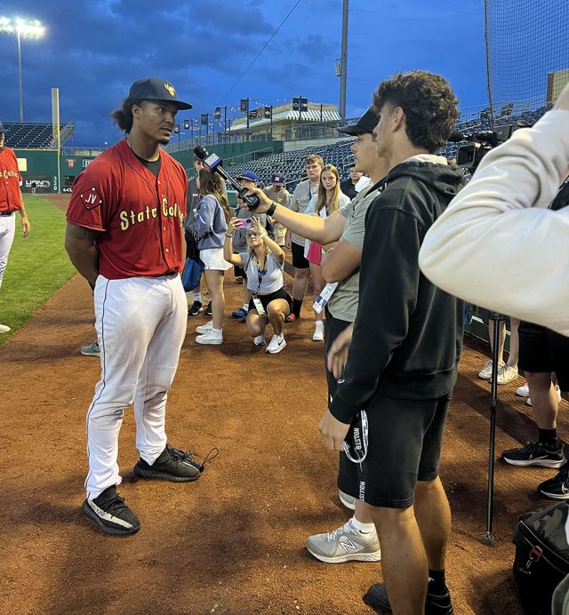 Students with a camera interview a baseball player.