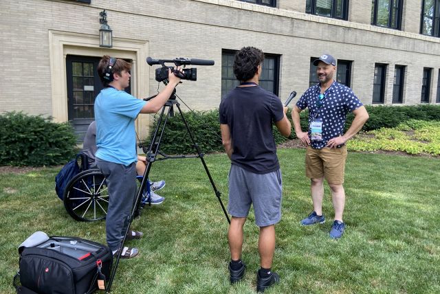 Four people with a camera on a grassy area for an interview.