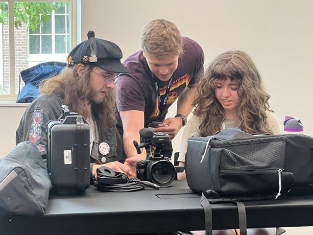 Three students talking about a camera