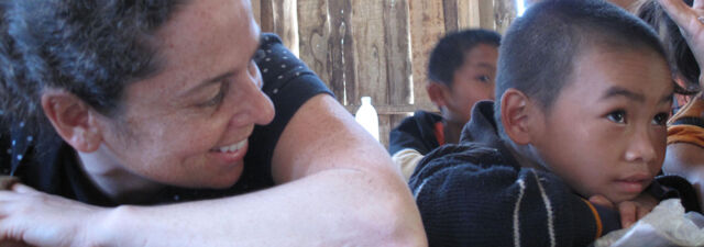 A researcher and a young boy have their heads resting on their arms and are smiling