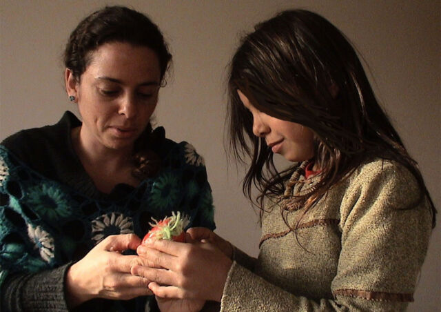 Two women share holding a piece of fruit while talking.