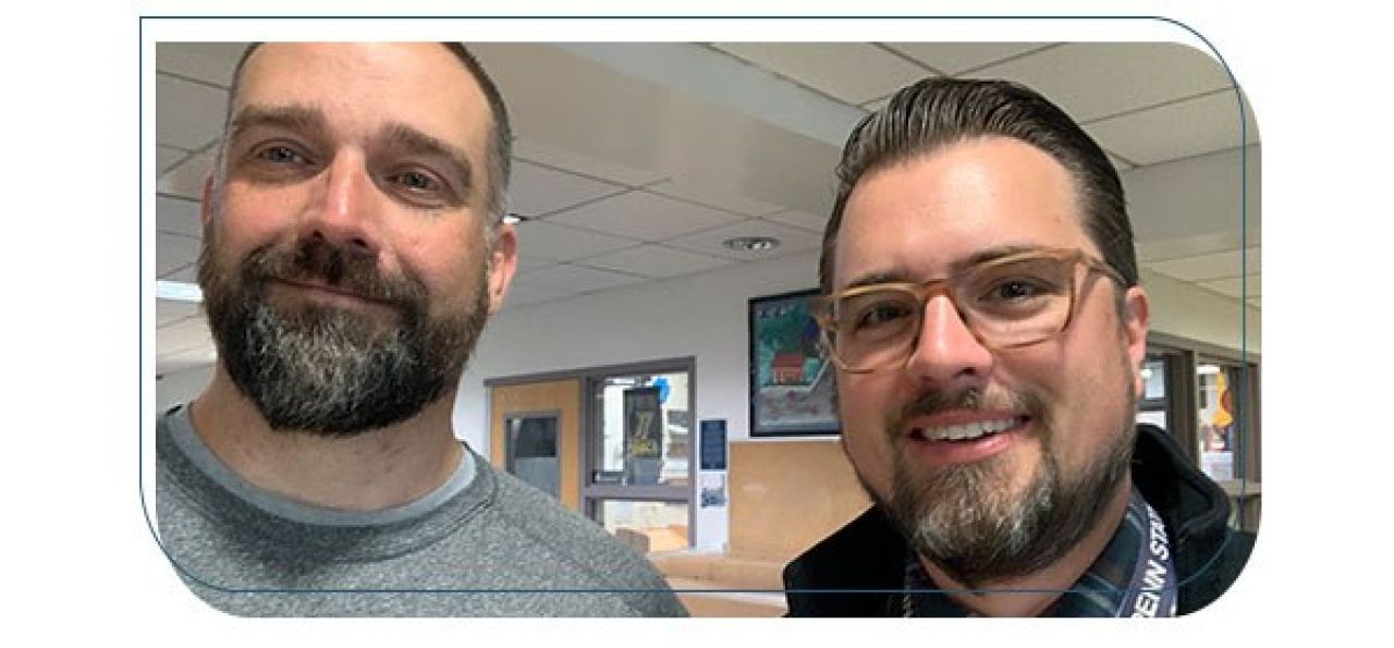 close up of two men, left is a man with a dark beard, right is a man with black hair and glasses