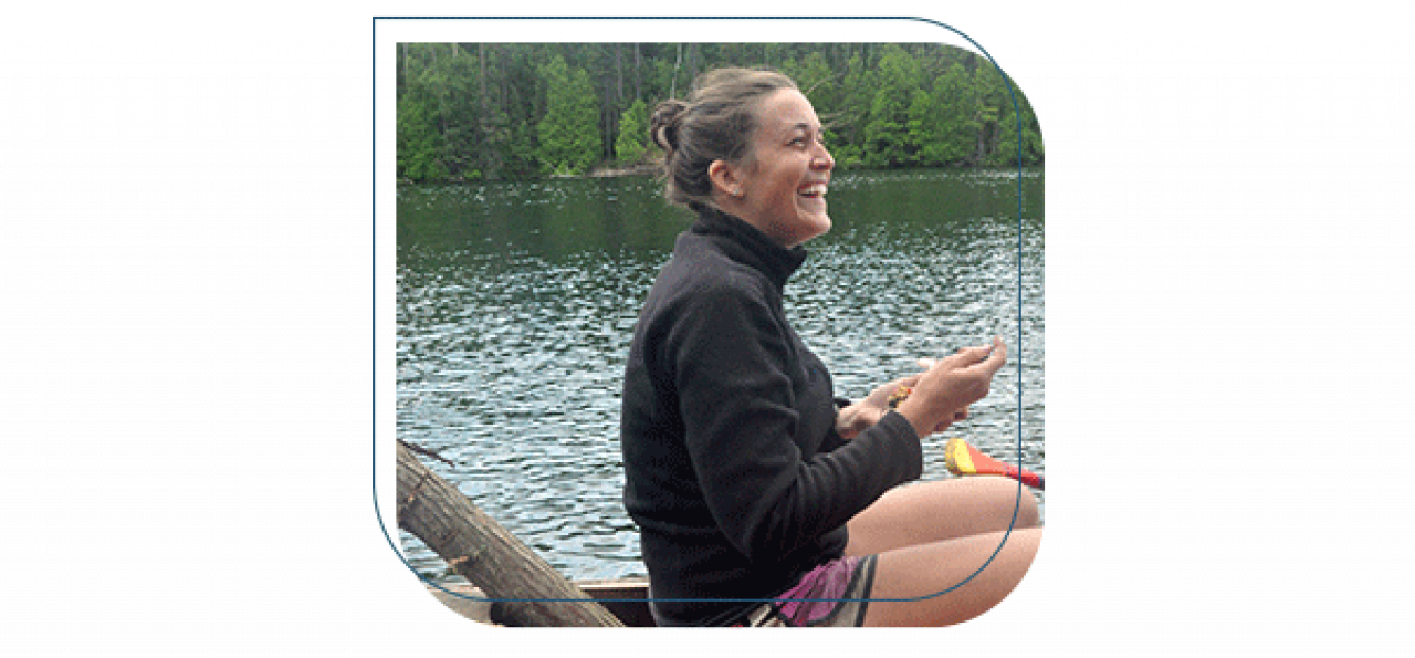 Woman sitting wearing a black fleece and pink shorts in canoe on a lake