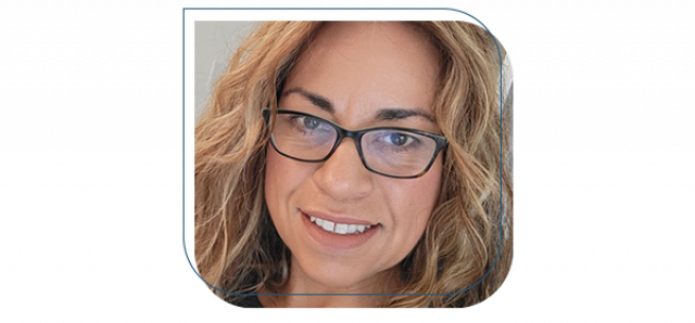 A woman wearing black-framed eyeglasses poses for a self photo. Her head and neck are visible, and she is smiling.