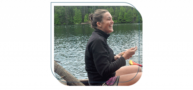 Woman sitting wearing a black fleece and pink shorts in canoe on a lake