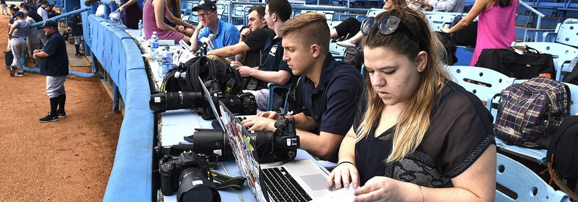 Two Penn State sports journalism students in the press box alongside a baseball field typing up notes on their laptops for stories about the Penn State baseball team playing in Cuba over Thanksgiving Break in 2015.