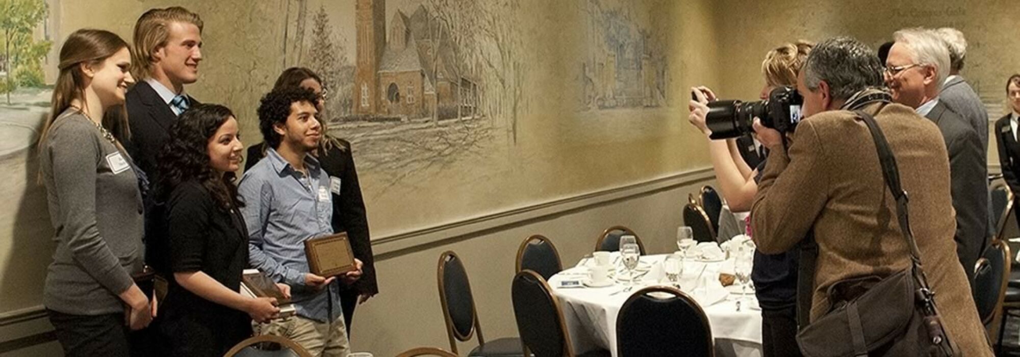 Five students stand in a banquet hall holding award plaques at the Davis Awards ceremony.