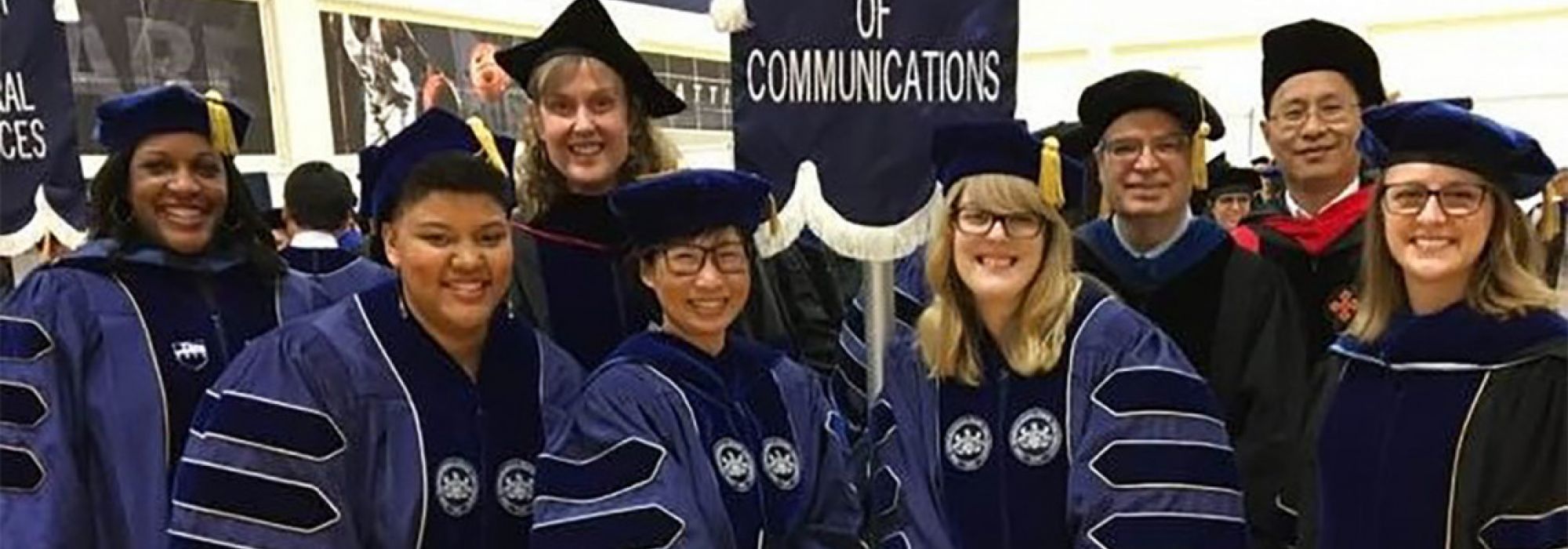 Four graduate students pose on graduation day in front of the college banner with their advisors.