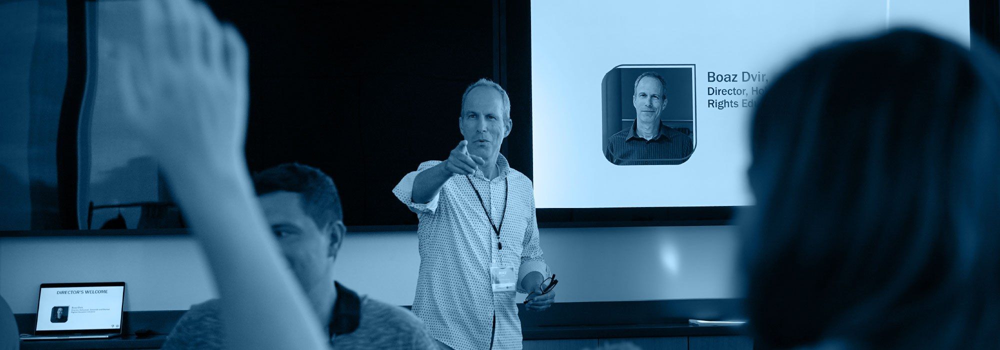 Man speaking to audience behind a blurred raised hand.