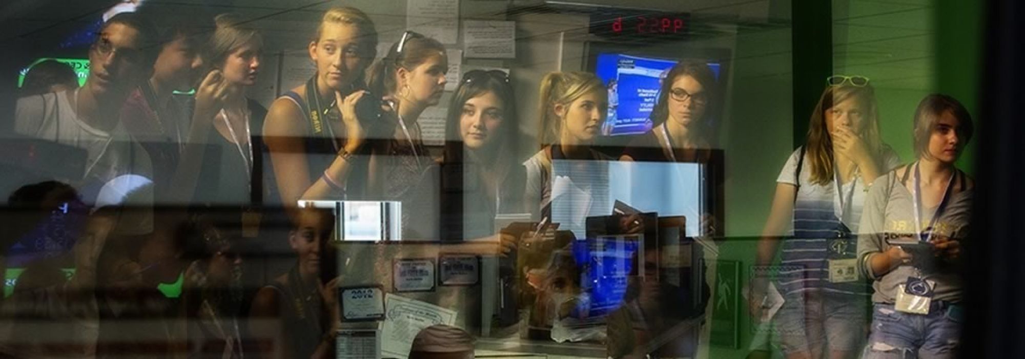 A bunch of young students with cameras and notebooks are creatively photographed in the reflection of a glass window.