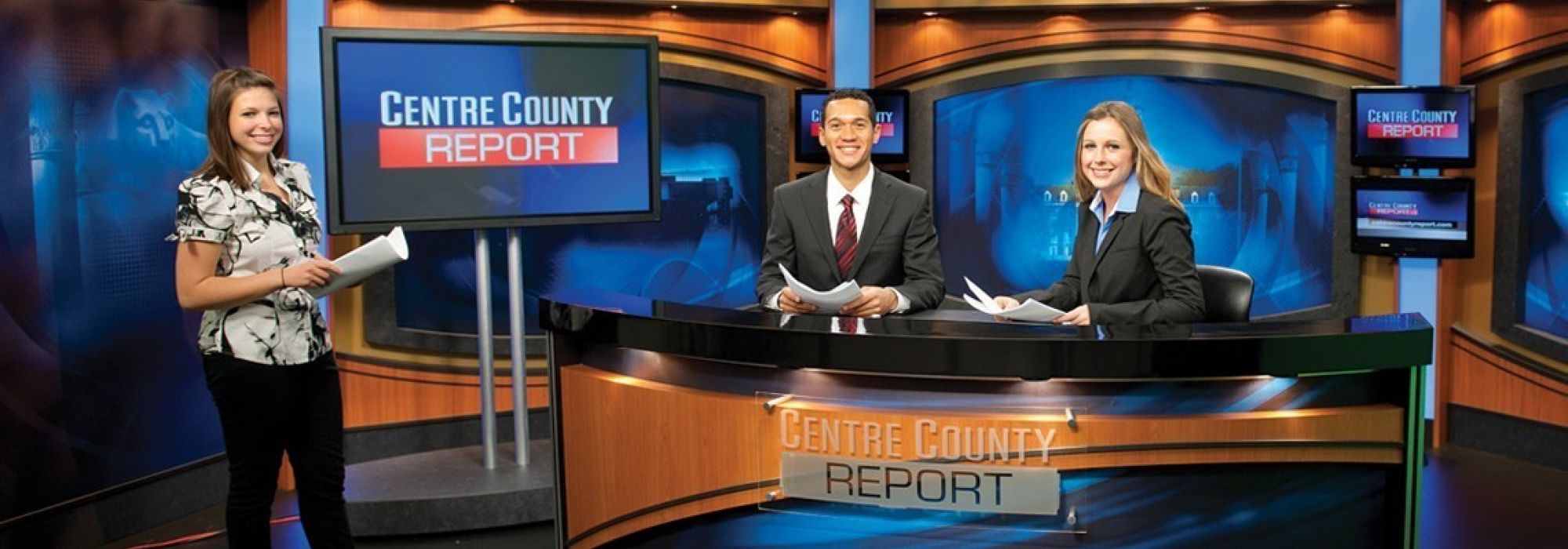 Three journalism students pose on the set for the tv news program, Centre County Report.