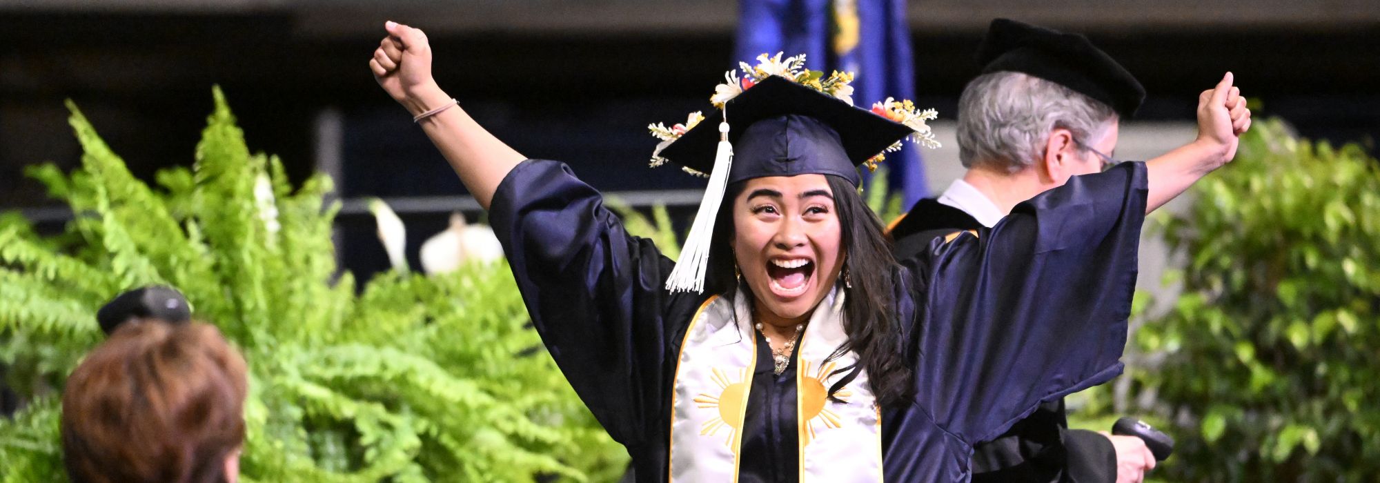 A student celebrates with arms outstretched while walking across the stage at commencment.