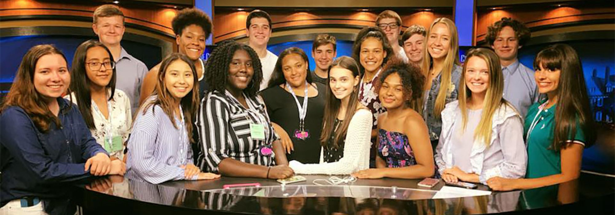 Eighteen young students stand behind the newsdesk on the set of Centre Country Report