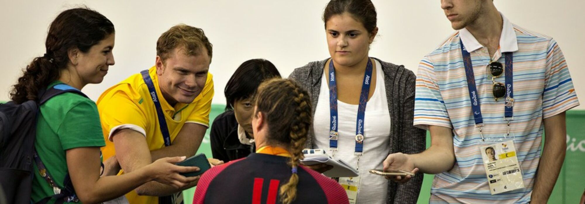 Five Penn State sports journalism students with press credential badges and recording audio on their mobile phones stand interviewing a paralympic athlete during the 2016 Paralympics
