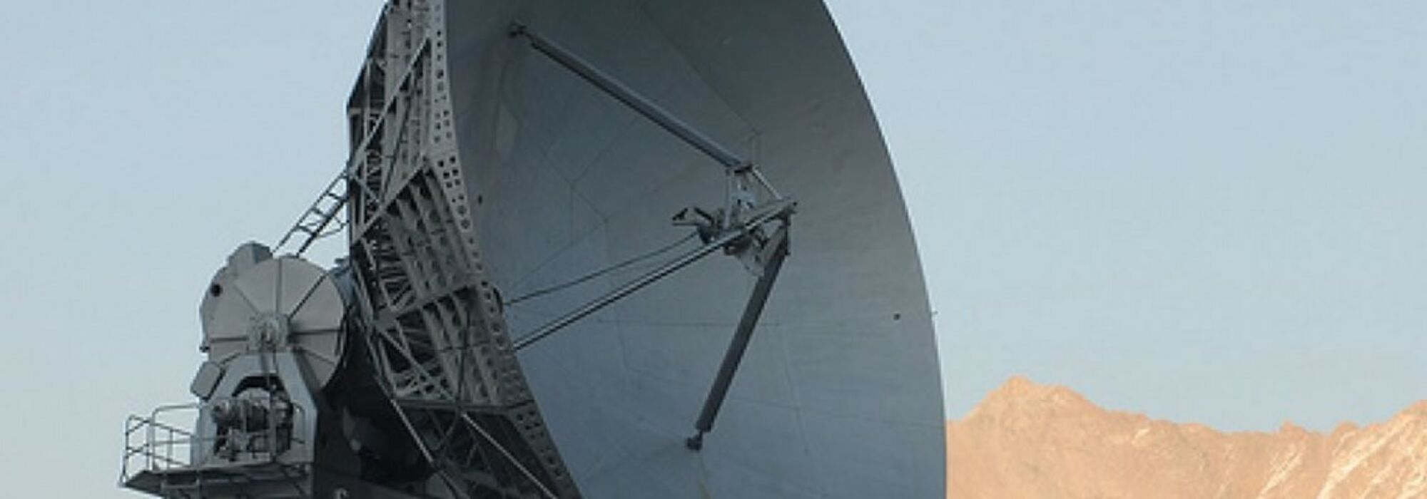 Satellite dish with a blue sky and desert mountain landscape in the background.