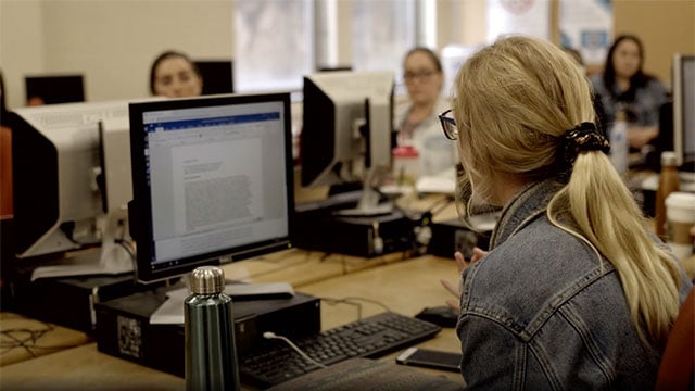 Students gathered around computers in a classroom writing workshop