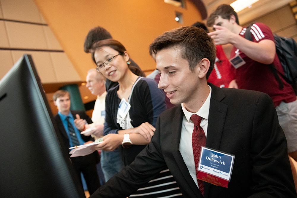 A student dressed in suit and tie demos a project on his computer for a faculty reviewer.