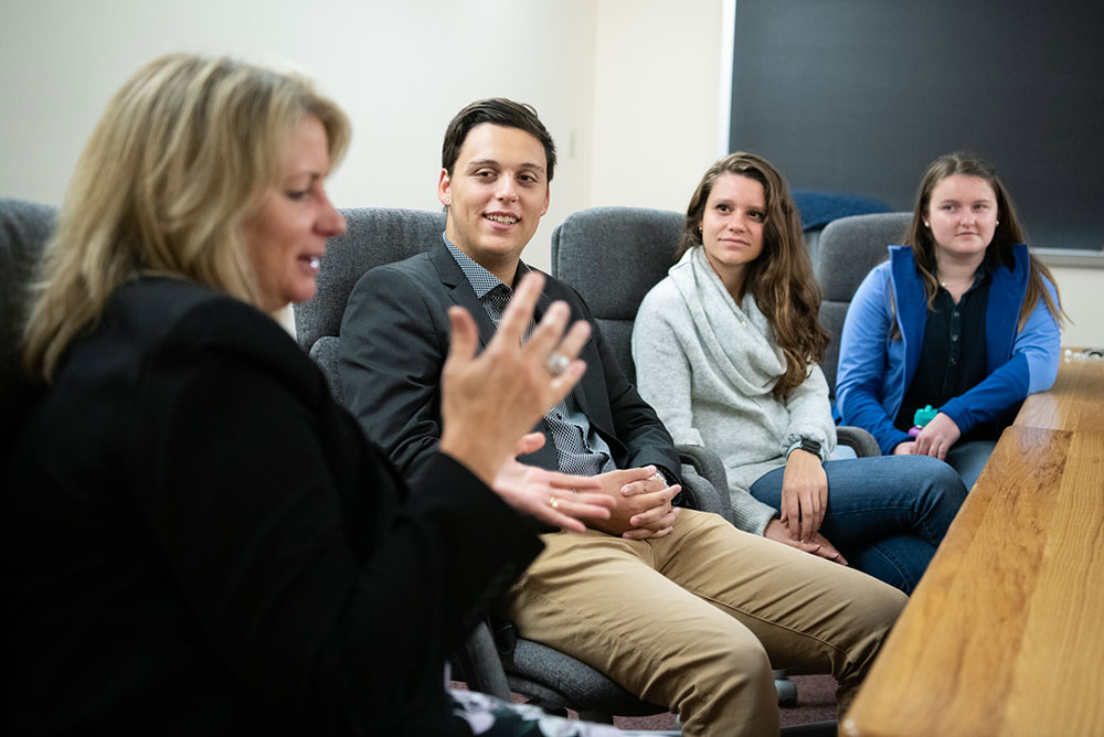 Soft focus photo of a blond woman talking to several students around a conference table.