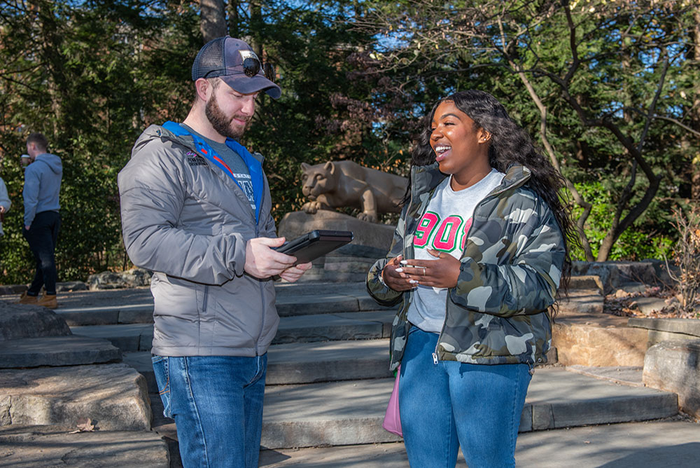 A student on a tablet running a survey asks questions of another student with the lion shrine in the background.