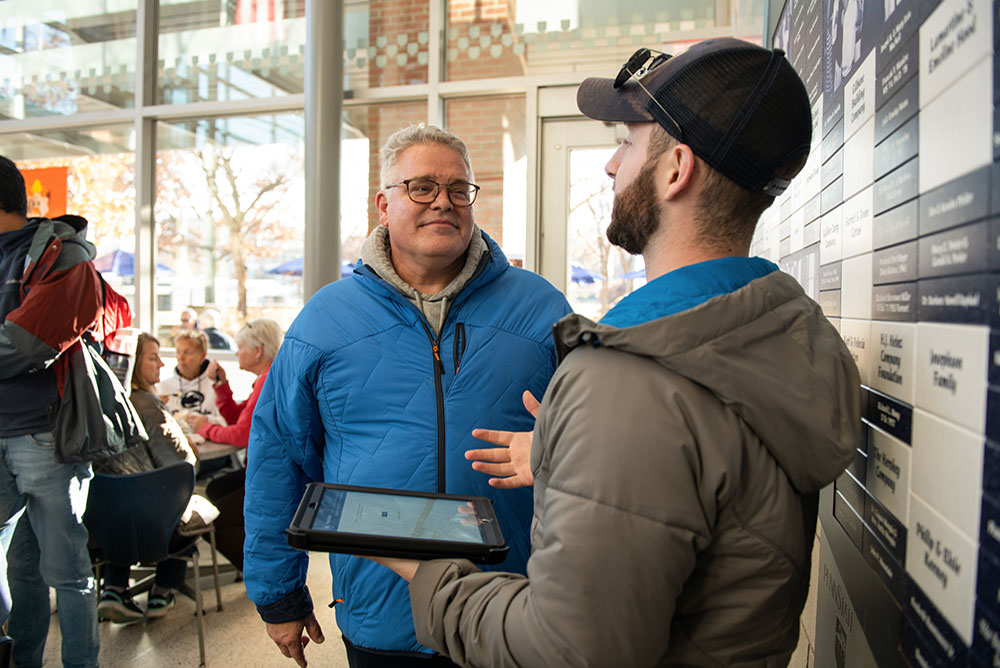 A student on a table running a survey and asking questions of a faculty member at the Berkey Creamery.