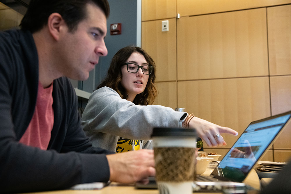 Two CommAgency social media strategists huddle around computers to discuss a new project