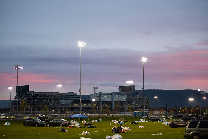 A view of Beaver Stadium as the sunrises on the day after a game. Trash and recyclables litter the ground in the parking lot.