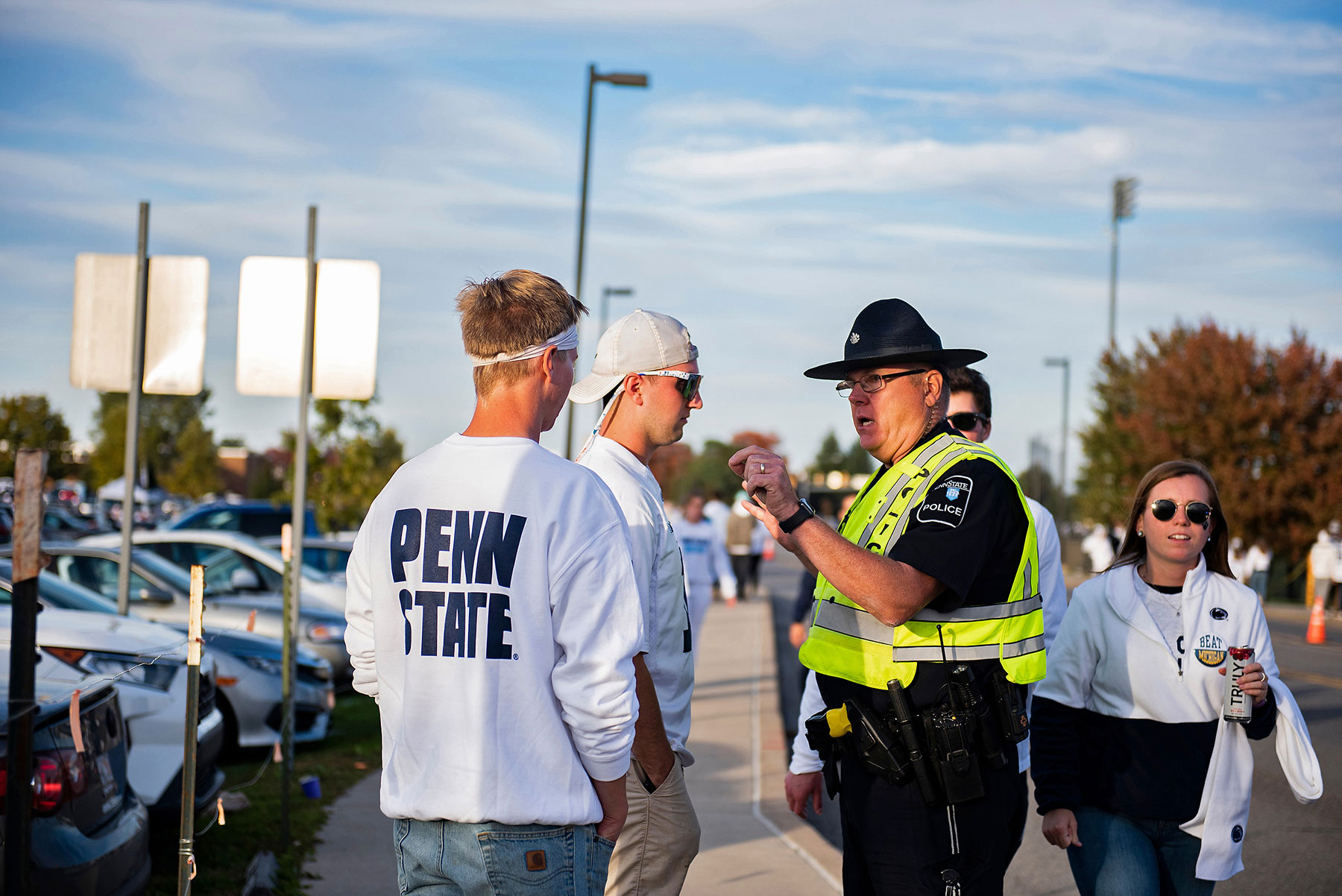 A police officer reprimanding two fans dressed in Penn State sweatshirts.