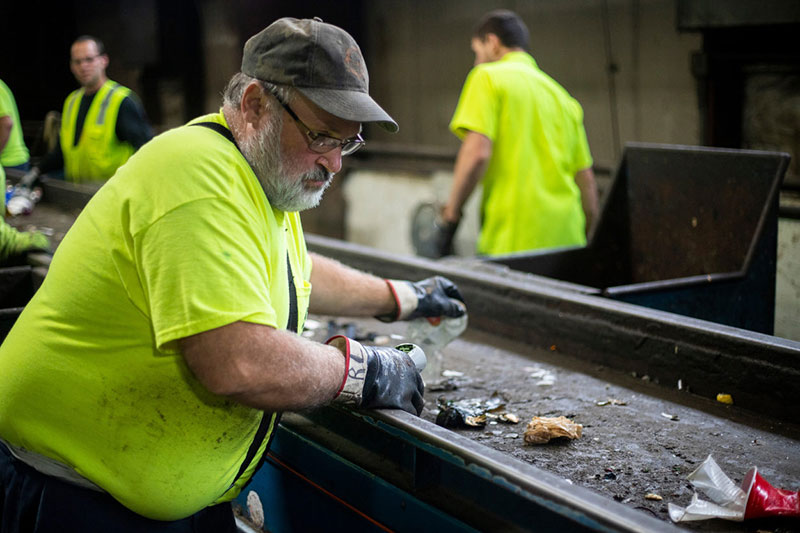 A worker sorts recycling as it cruises by on a conveyor belt.