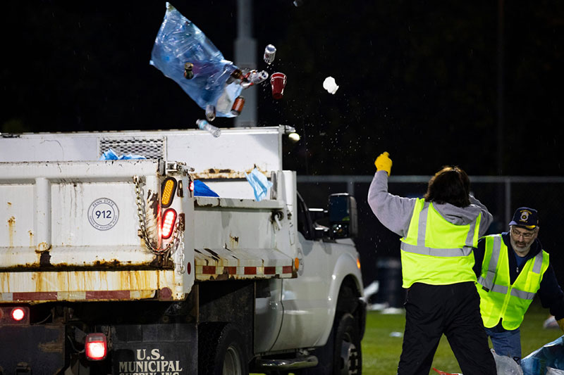 A worker throws a bag of recylables into the back of a white work truck.