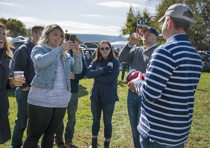 Fans taking photos and drinking beer at a tailgate.