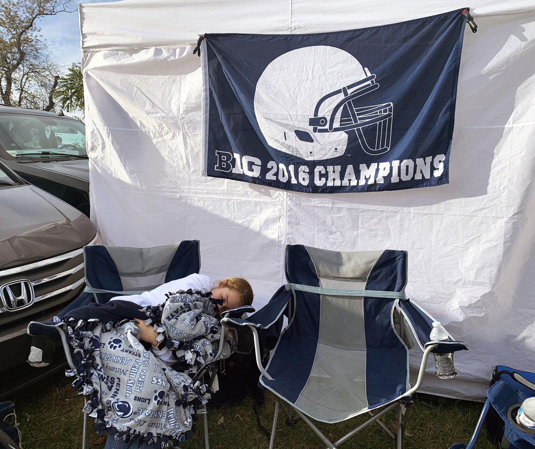 A young fan under a fleece Penn State blanket curls up in a camping chair for a quick nap during tailgating.