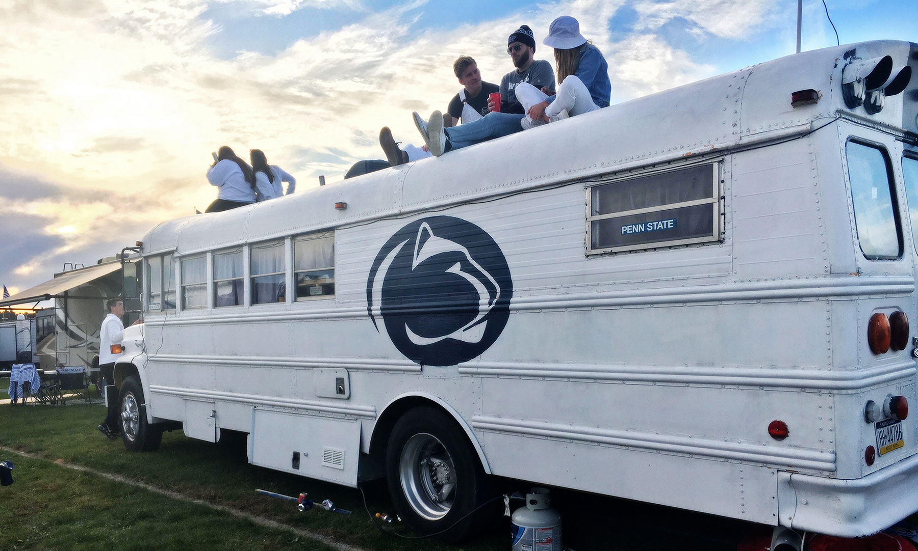 Several fans sitting on top of a white school bus with a big
Penn State logo on its side.