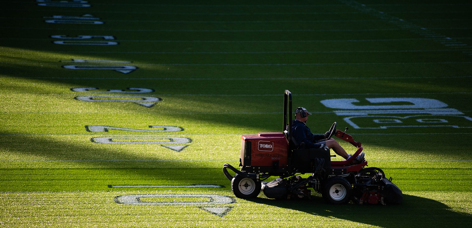 A groundskeeper riding a red Toro lawnmower mows grass along the 10 yard line at Beaver Stadium.