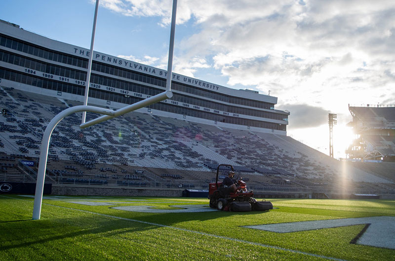 The sun sets over the endzone at Beaver Stadium while a riding mower trims the grass.