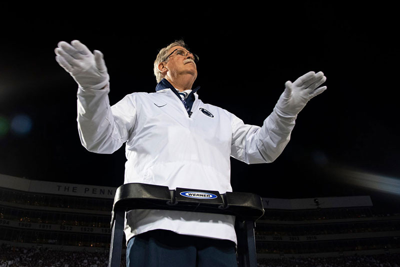 Dave Cree standing at the top of a ladder conducting the Blue Band during a game.