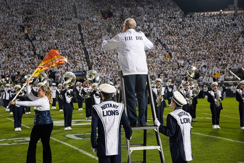 Dave Cree standing at the top of a ladder conducting the Blue Band during a game.
