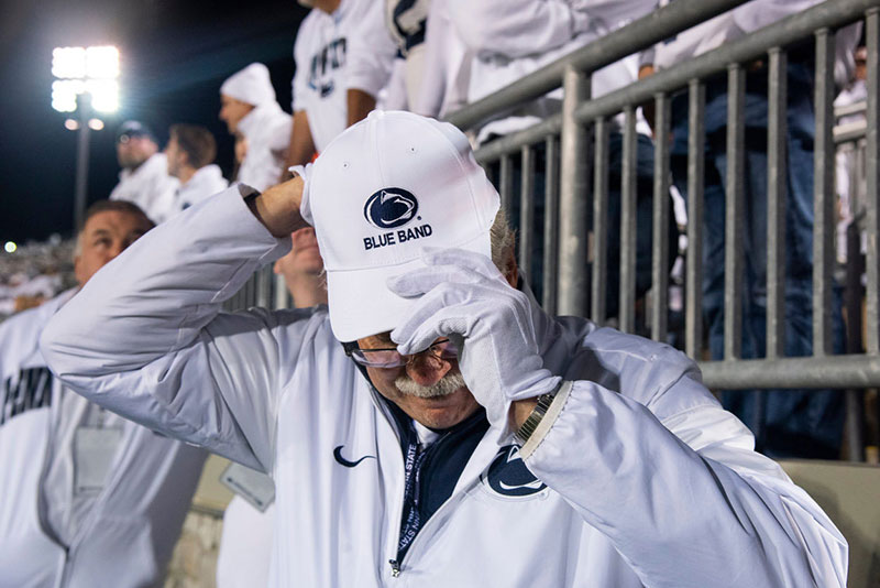 Dave Cree dressed in a white Penn State jacket adjusts his baseball hat.