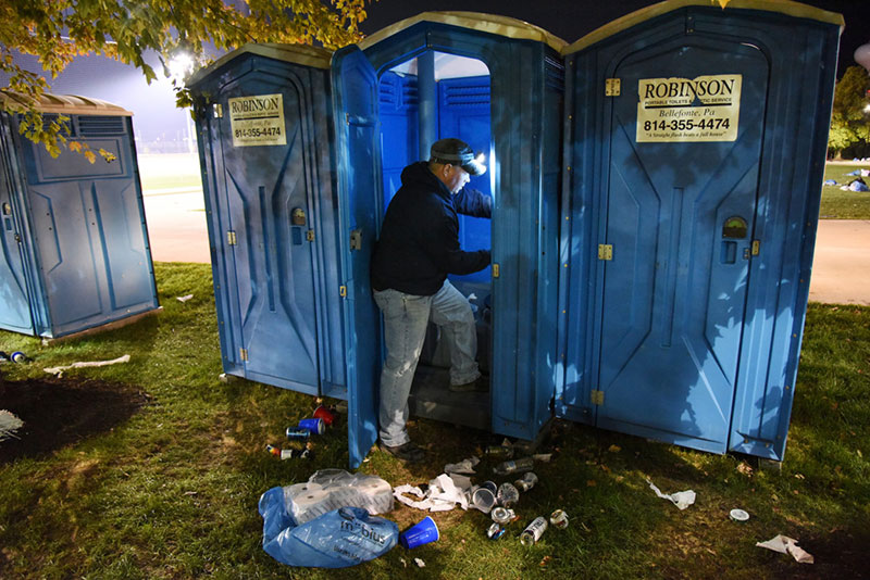 A septic system worker restocks toilet paper in a portable toilet outside Beaver Stadium