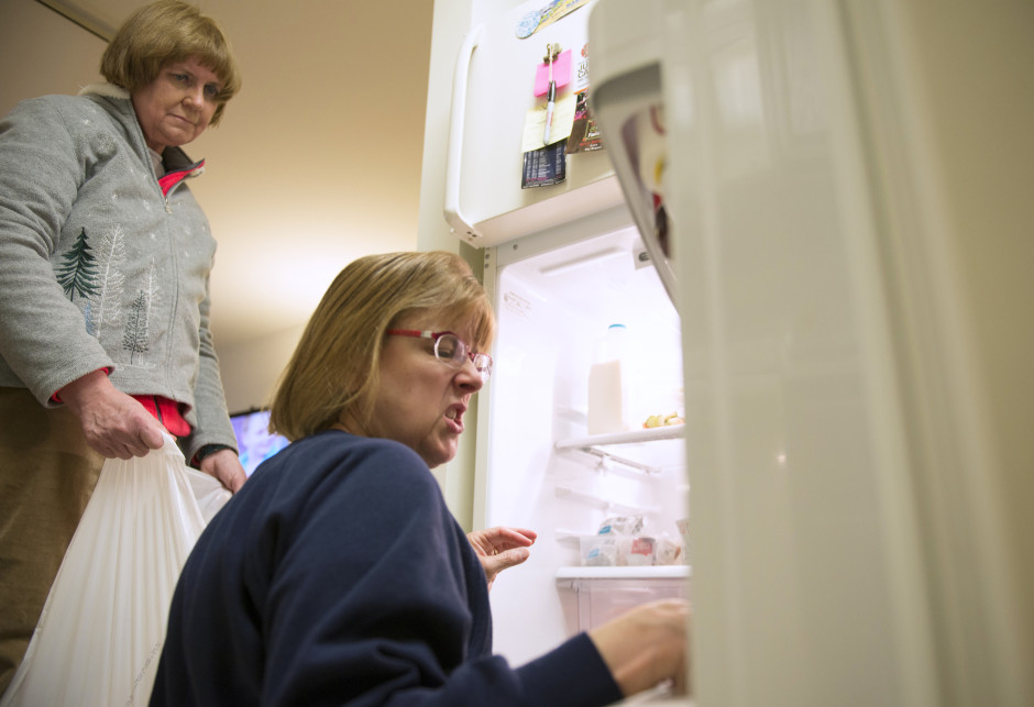 Lisa Bendarchik kneels in front of a refrigerator cleaning out spoilded food.