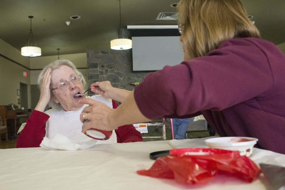 Lisa helping her mother eat by spoon feeding her soup.