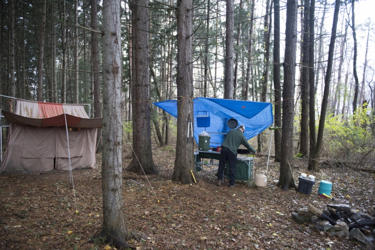 Zack standing under a blue tarp brewing coffee in the morning.